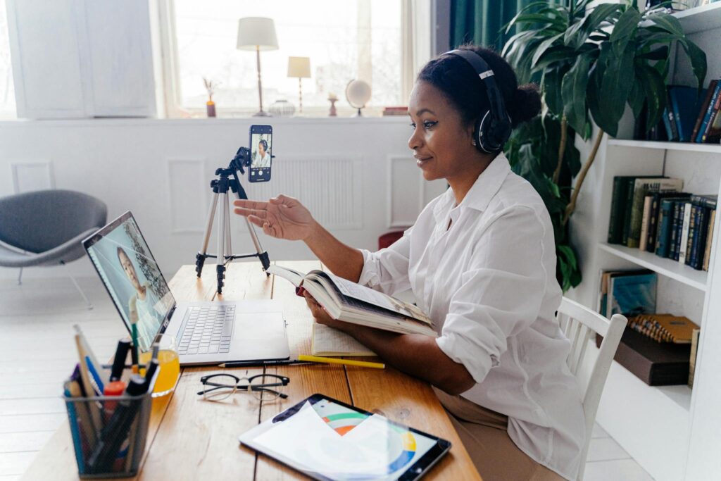 Woman engaged in a video conference, working remotely with laptop and tablet in a cozy home office.